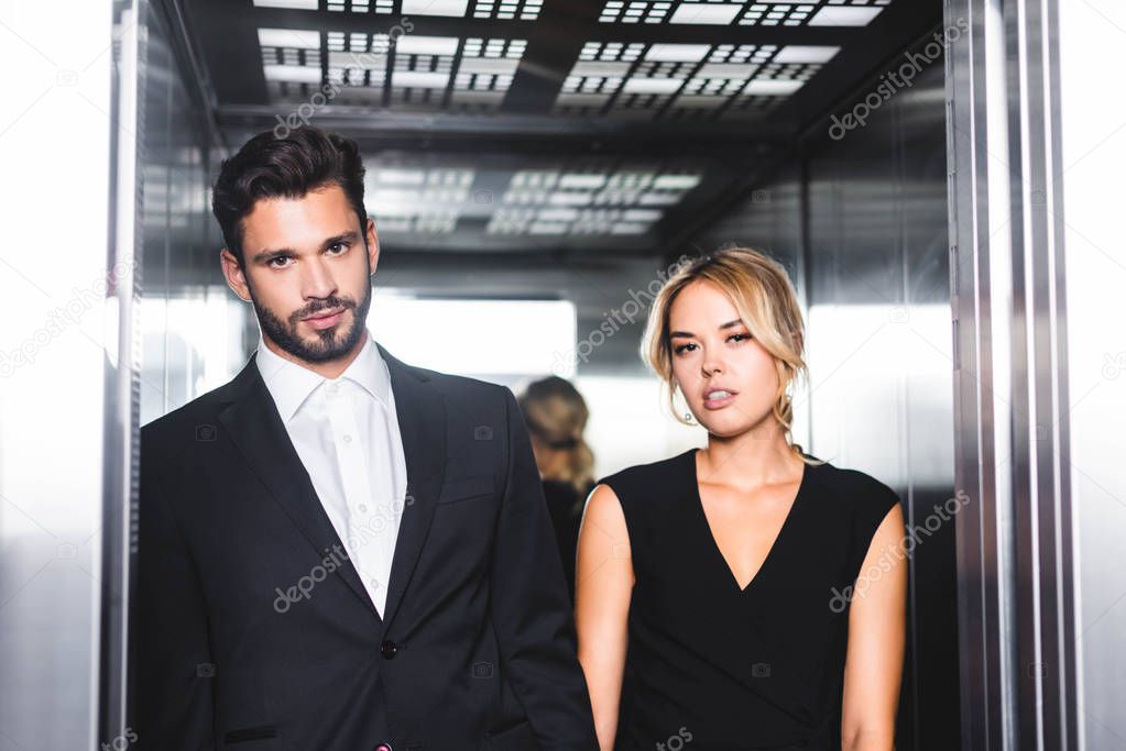 Business couple looking at camera in office elevator 