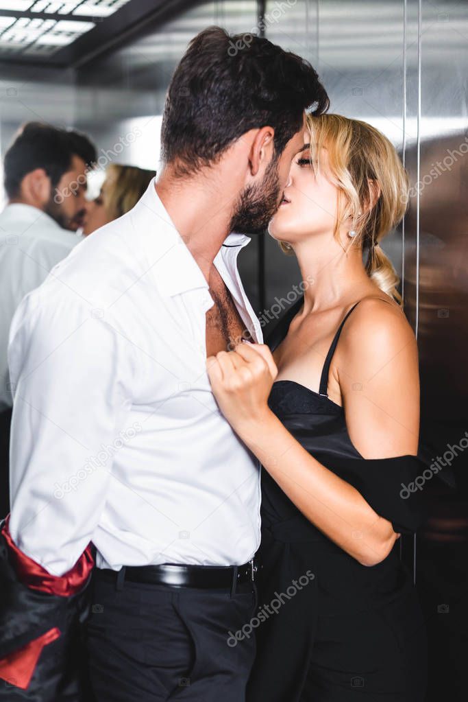 Businessman taking off jacket while kissing sexy woman in office elevator