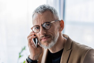 Gözlüklü yakışıklı ve sakallı iş adamı akıllı telefondan konuşuyor. 