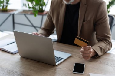 Bilgisayarın yanında kredi kartı tutan işadamlarının görüntüsü ve boş ekranlı akıllı telefon. 