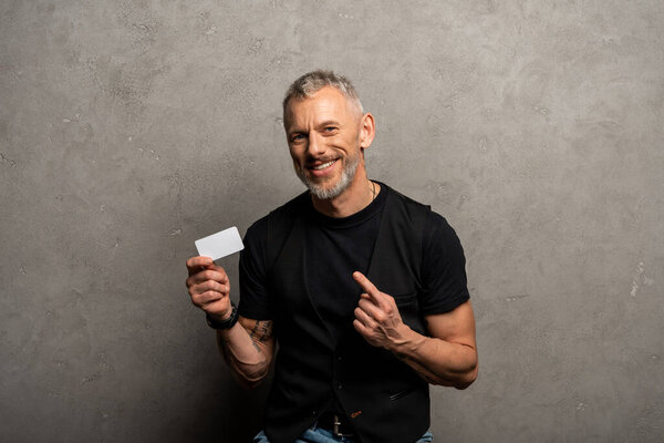 happy businessman pointing with finger at blank card on grey 