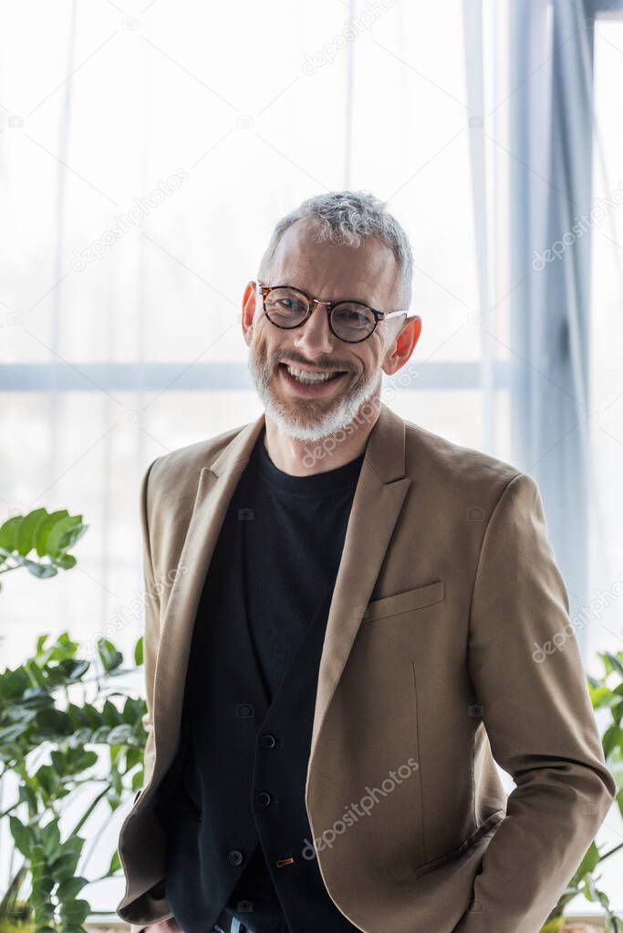 cheerful businessman in glasses smiling while standing in office 