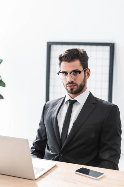 Handsome businessman in eyeglasses looking at camera at workplace — Stock Photo