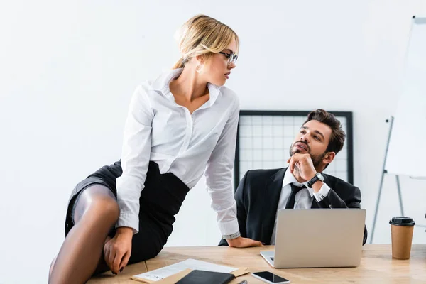 Sexy secretary sitting on table while flirting with businessman — Stock Photo