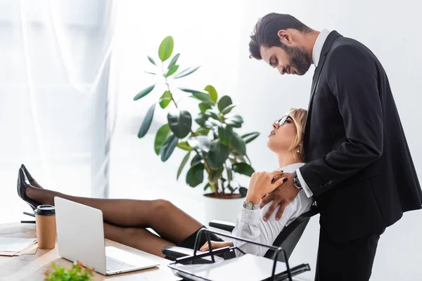 Vista laterale dell'uomo d'affari che abbraccia un collega sexy dal posto di lavoro in ufficio — Foto stock