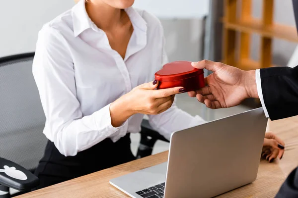 Vista recortada del hombre de negocios dando caja de regalo a la mujer en la oficina - foto de stock