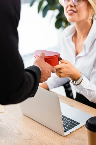 Selective focus of businessman giving gift to smiling colleague in office — Stock Photo