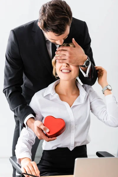 Geschäftsmann hält Geschenkbox in der Hand und verdeckt lächelnden Kollegen die Augen — Stockfoto