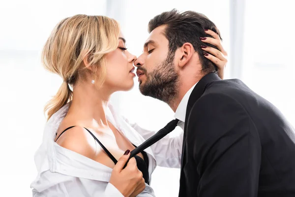 Vista lateral de empresária sexy puxando colega gravata enquanto flerta no escritório — Fotografia de Stock