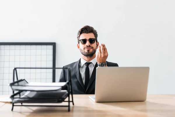 Schöner Geschäftsmann mit Sonnenbrille gestikuliert am Bürotisch — Stockfoto