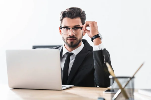 Hombre de negocios guapo ajustando las gafas mientras usa el ordenador portátil - foto de stock