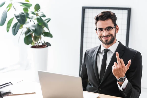 Lächelnder Geschäftsmann zeigt Mittelfinger-Geste am Bürotisch — Stockfoto
