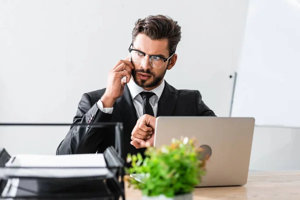 Handsome businessman talking on smartphone at office table — Stock Photo