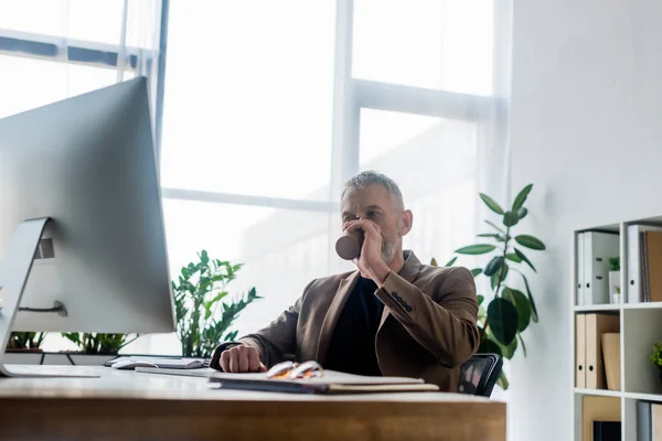 Selective focus of businessman drinking coffee to go near computer monitor — Stock Photo