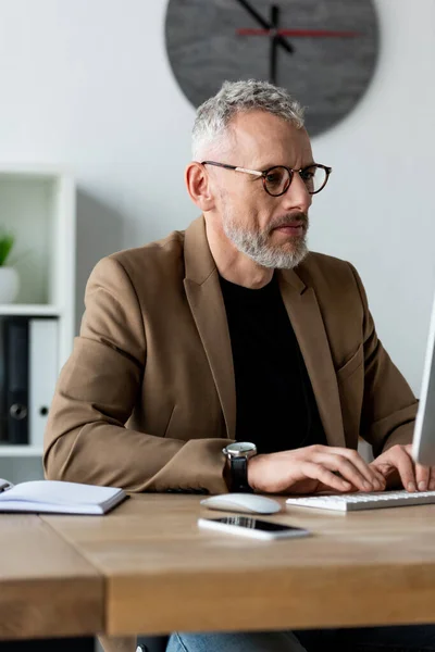 Selektiver Fokus des Geschäftsmannes in Brille tippt auf Computertastatur in der Nähe des Smartphones — Stockfoto