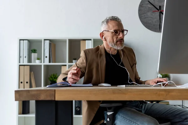 Handsome businessman in earphones looking at computer monitor in office — Stock Photo