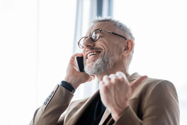 Selektiver Fokus des glücklichen und bärtigen Geschäftsmannes, der auf dem Smartphone spricht und den Daumen nach oben zeigt — Stockfoto