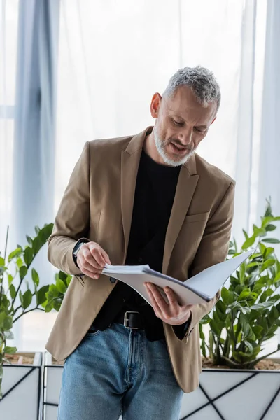 Bärtiger Geschäftsmann schaut sich Dokument an, während er Ordner im Büro hält — Stockfoto