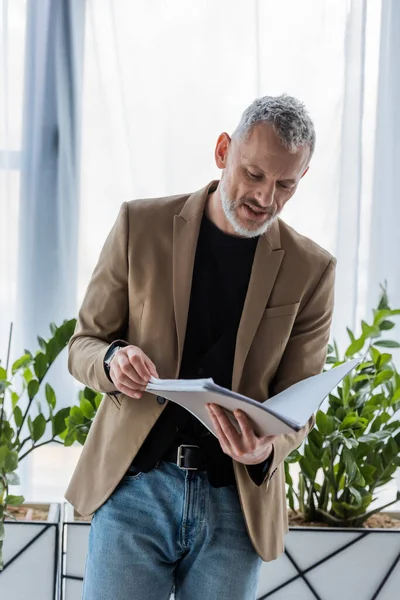 Hombre de negocios barbudo mirando el documento mientras sostiene la carpeta en la oficina - foto de stock