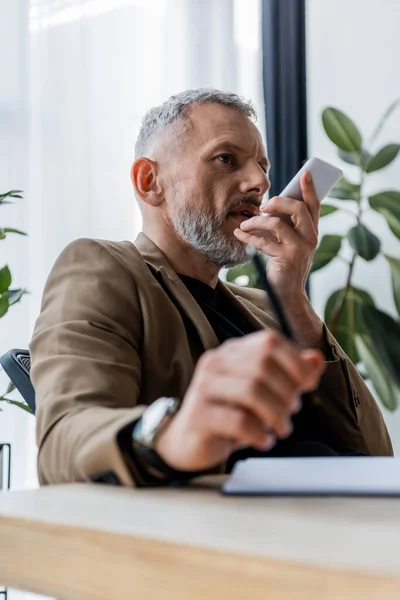 Selective focus of bearded businessman recording voice message while holding smartphone — Stock Photo