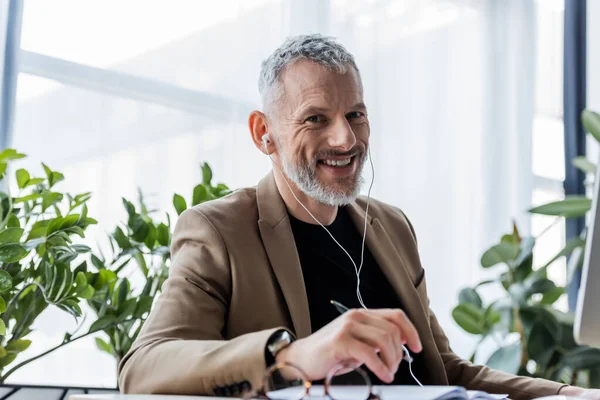 Selektiver Fokus glücklicher Geschäftsleute mit Kopfhörern, die in die Kamera im Büro schauen — Stockfoto