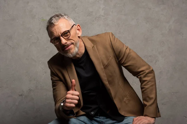 Happy businessman in glasses looking at camera and showing thumb up on grey — Stock Photo