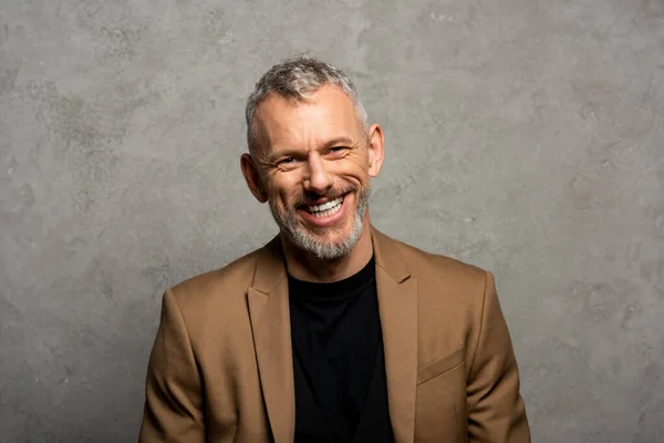 Cheerful businessman in blazer looking at camera on grey — Stock Photo