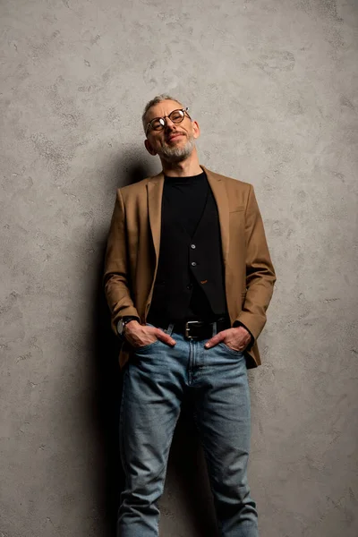 Schöner Geschäftsmann mit Brille, die Hände in den Taschen auf grau — Stockfoto