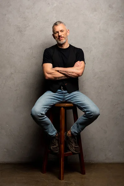 Uomo barbuto con braccia incrociate seduto su sgabello grigio — Foto stock