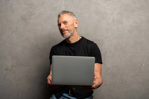 Handsome man using laptop and looking at camera on grey — Stock Photo