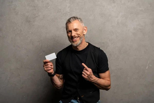 Щасливий бізнесмен вказує пальцем на порожню картку на сірому — стокове фото