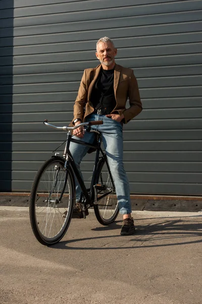 Luce del sole sul bell'uomo d'affari con mano in tasca vicino alla bicicletta fuori — Foto stock