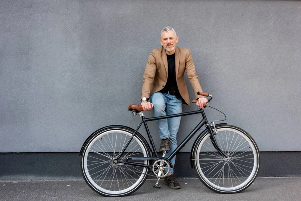Bonito empresário em blazer e jeans de pé perto de bicicleta fora — Fotografia de Stock