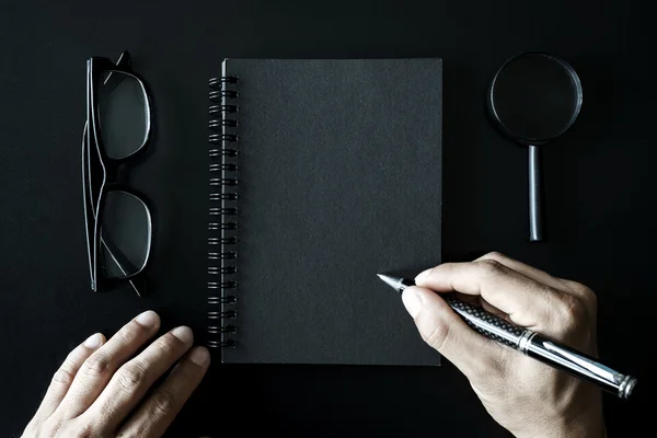 Caderno preto com copyspace em fundo preto e mão writi — Fotografia de Stock