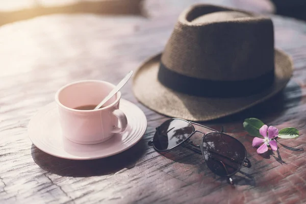 Hatt med solglasögon och kopp kaffe på träbord — Stockfoto