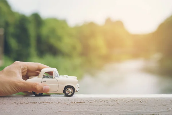 Mão segurando um carro com paisagem de fundo — Fotografia de Stock