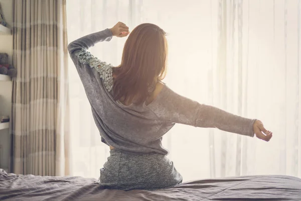 Frau streckt Arme aus und wacht auf dem Bett sitzend auf — Stockfoto