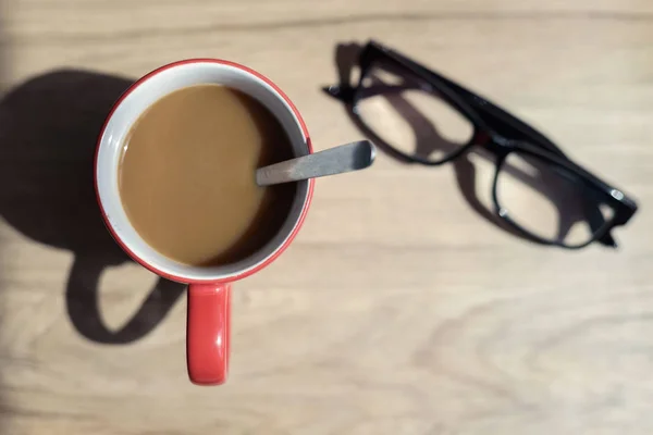 Kopp kaffe och glasögon med skugga på trä skrivbord — Stockfoto