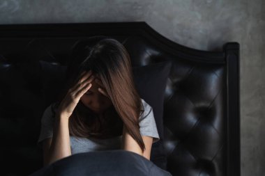 Yalnız genç bir kadın, karanlık yatak odasında otururken depresyonda ve stresli, negatif duygu konsepti.