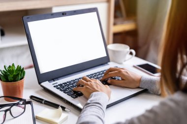 Oturma odasında oturan genç bir kadın evde dizüstü bilgisayar ve akıllı telefon üzerinde çalışıyor.