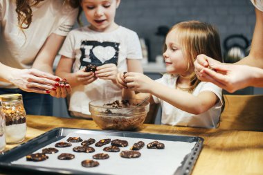 Mutfakta yemek pişiren mutlu anne ve iki kızın portresi.