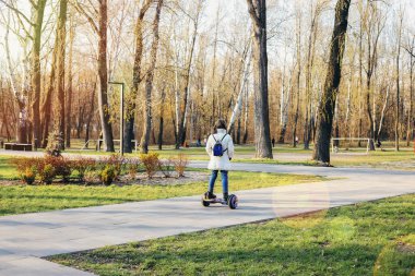 Uçan bir çocuk. Çocuklar bahar parkında scooter kullanıyor. Çocuklar için denge tahtası. Okul çocuğu için modern aletler.