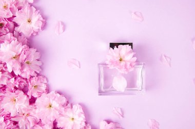 Pembe arka planda sakura çiçekleri olan bir şişe parfüm.