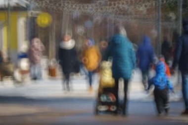 Arka plan bulanık. Çocuğu olan bir anne şehir caddesi boyunca yürür. Şehir hayatı. İnsan siluetleri. Aile tatili.