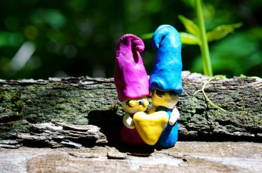 Kil içinden bir kalp tutan iki cüce. Ahşap bir arka planda peri figürleri.