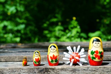 Bir sıra tahta oyuncak bebek. Aralarında bir virüsün plastik figürü var..