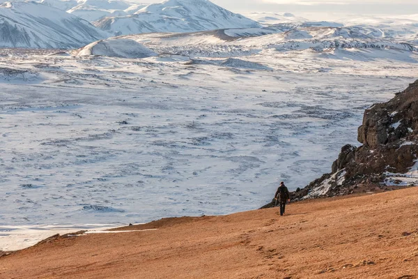 Um homem caminhando sobre uma superfície vermelha para um vulcão no inverno. Islândia . — Fotografia de Stock