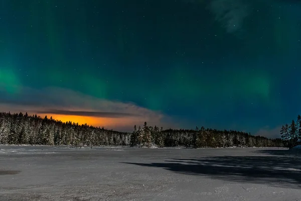 Luces polares dramáticas, Aurora boreal con muchas nubes y estrellas a la luz de la luna en el cielo sobre un lago congelado y un bosque nevado en Suecia. larga velocidad de obturación . — Foto de Stock