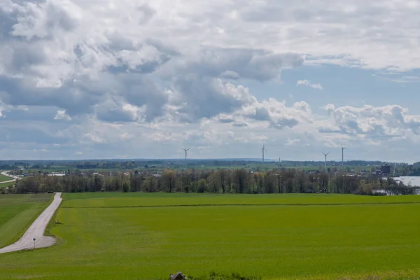 Θυελλώδης ουρανός πάνω από ένα πράσινο σπαρμένο πεδίο με αιολική ενέργεια στο παρασκήνιο. Κεντρική Σουηδία. — Φωτογραφία Αρχείου