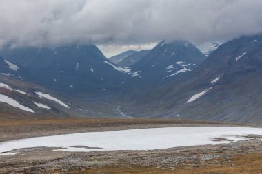 İsveç Laponya 'daki Sarek ulusal parkının güzel vahşi doğası. Karlı dağ zirveleri, nehir ve göl, huş ağacı ve çam ağaçları ormanı. Fırtınalı havada sonbahar renkleri. seçici odak
